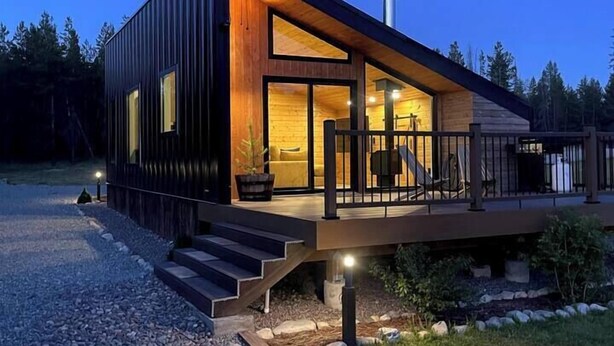 Une cabane en bois moderne dotée d’une terrasse, de grandes fenêtres et d’une cheminée.