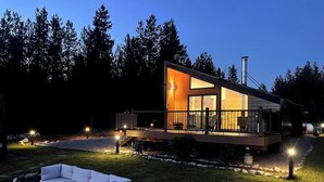 Une maison moderne dotée d’une façade en verre, d’une terrasse et d’un éclairage extérieur.