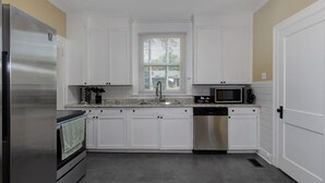 A compact kitchen with white cabinets, a stainless steel refrigerator, a microwave, and a dishwasher. - Pet-Friendly Home by Trail & Base (Columbus)