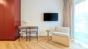 A modern room with a red wardrobe, a sofa, a TV mounted on the wall, and a small table with chairs. - Czysta Chic Harmony Studio (Wrocław)