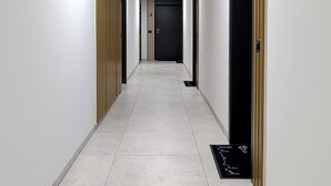 A corridor with a tiled floor, a door at the end, and a light fixture on the ceiling. - Czysta Chic Harmony Studio (Wrocław)