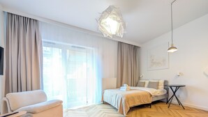 A modern hotel room with a large bed, a sofa, a small table, and a unique ceiling light fixture. - Czysta Chic Harmony Studio (Wrocław)