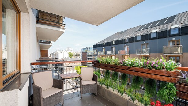 Een balkon met rieten stoelen, een tafel en een bloembak met bloemen.