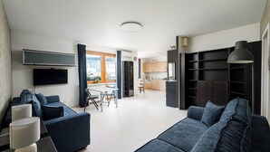 Een moderne woonkamer met een grote bank, een flatscreen televisie en een eethoek met een tafel en stoelen.