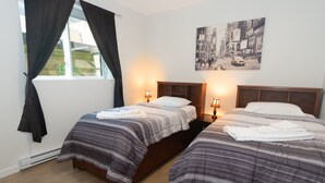 A double room with two beds, a window with curtains, a wall-mounted picture, and bedside lamps. - Kam Residence  (Chilliwack)