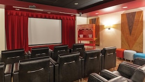 Un cine con filas de asientos de cuero negro, un telón rojo de fondo, una pantalla blanca y un puesto de palomitas.