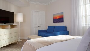Una habitación de hotel con una cama, un sofá azul, un televisor, un aparador y un cuadro de una puesta de sol.
