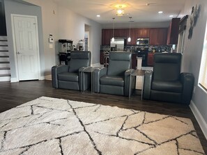 A living room with dark wood flooring, a beige rug, and three black leather chairs.