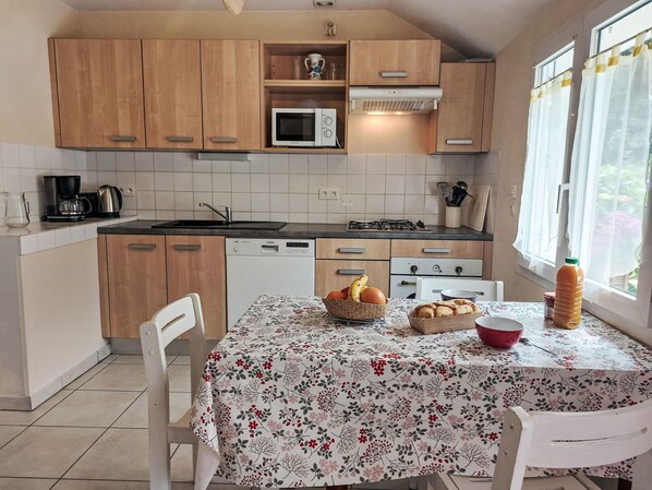 A kitchen with wooden cabinets, a microwave, a gas stove, and a dining table with a floral tablecloth.