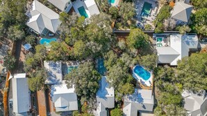 Vue aérienne d’un quartier résidentiel composé de plusieurs maisons, chacune dotée d’une piscine entourée d’arbres.