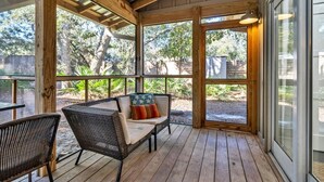 Un patio couvert doté d’un plancher en bois, de meubles en osier et de grandes fenêtres offrant une vue sur l’extérieur.