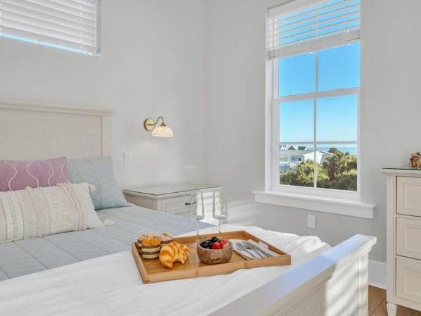 Quarto com cama, mesa de cabeceira, janela com persianas e bandeja com itens de café da manhã.