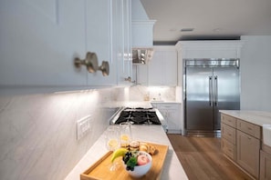 Cozinha moderna com armários brancos, eletrodomésticos de aço inoxidável e bancada de mármore.