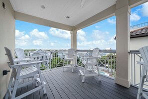 A covered outdoor deck with white chairs and a view of a residential area.