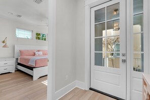 Quarto com cama, mesa de cabeceira e porta branca com painéis de vidro.