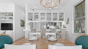 Un coin repas avec une table en bois, des chaises blanches et un lustre.