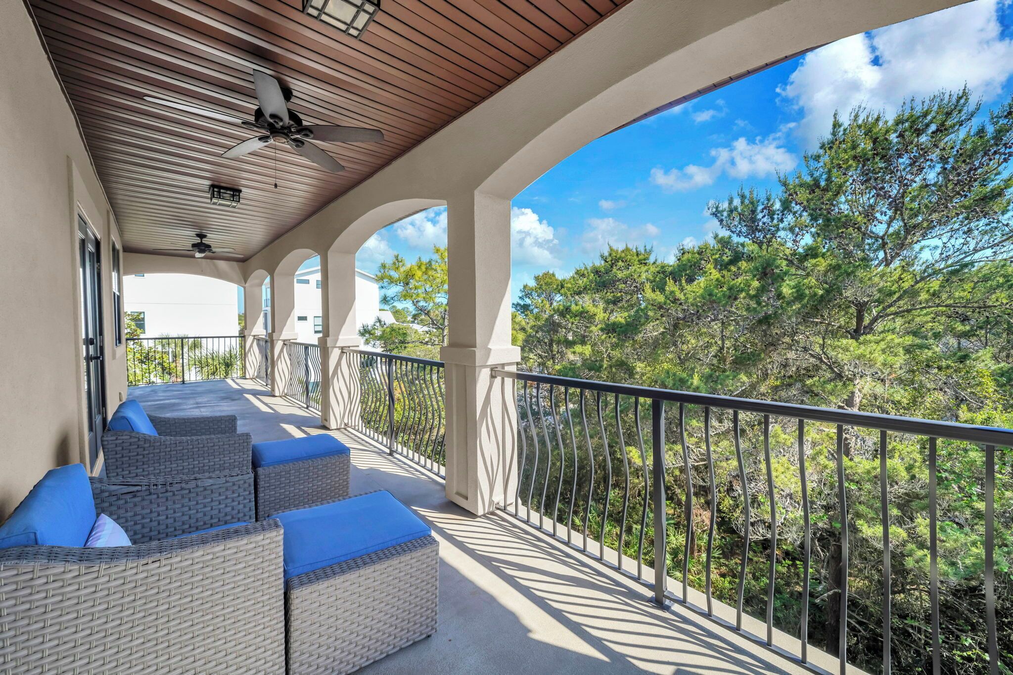 A covered balcony with wicker furniture and a railing overlooking a forested area.