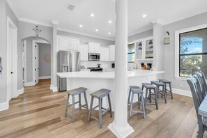 Une cuisine moderne avec des meubles blancs, un îlot central doté de tabourets et une grande fenêtre.
