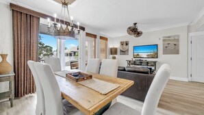 A dining area with a wooden table, white chairs, a chandelier, and a view of the outdoors. - Observation Pt N 252-4 at Baytowne Warf- Pool, Gym, and Large Private Balcony! (Miramar Beach)