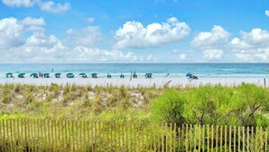 A beach with rows of beach chairs and umbrellas, a wooden fence, and a clear sky. - Emerald Towers West 1005- Beach Front with Gulf View Balcony! (Fort Walton Beach)