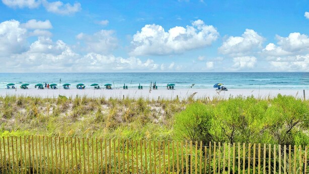 A beach with rows of beach chairs and umbrellas, a wooden fence, and a clear sky. - Emerald Towers West 1005- Beach Front with Gulf View Balcony! (Fort Walton Beach)