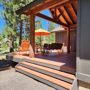 Una terraza de madera con mobiliario exterior, incluyendo sillas y una mesa, bajo un espacio cubierto con techo de madera.