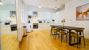 A modern kitchen with white cabinets, a central island with chairs, and a dining table.