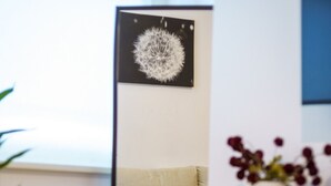 A room with a sofa, a mirror reflecting a dandelion art piece, a vase with flowers, and a wooden cabinet. - The Regent’s Park Nook - 1BR (Greater London)