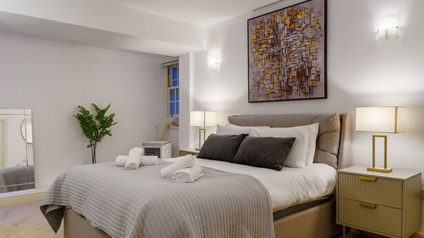 A modern bedroom with a large bed, bedside tables, a mirror, and a painting on the wall. - The Regent’s Park Nook - 1BR (Greater London)