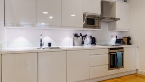 A modern kitchen with white cabinetry, a stainless steel microwave, and a coffee maker. - The Regent’s Park Nook - 1BR (Greater London)