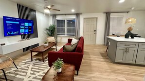 Een moderne woonkamer met een flatscreen televisie, een rode bank, een houten salontafel en een eethoek met een keukenbar.