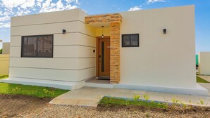 A modern two-story building with a flat roof, a central entrance with a wooden door, and a small overhang above the door. - villa mon Fleur w/jacuzzi,free shuttle at casa linda (Sosua)