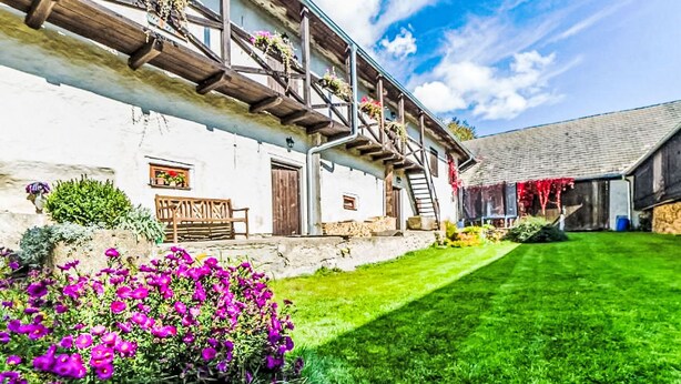 A rustic building with a wooden staircase, a bench, and a flower bed.