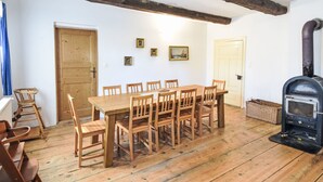 A dining area with a wooden table and chairs, a wooden floor, a wooden door, and a black wood stove.