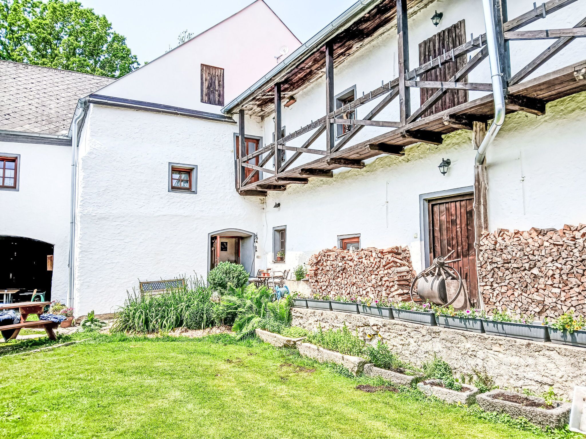 Ein traditionelles Gebäude mit weißer Fassade, hölzernen Balkonen und einem Gartenbereich mit Pflanzen und einer Holzbank.