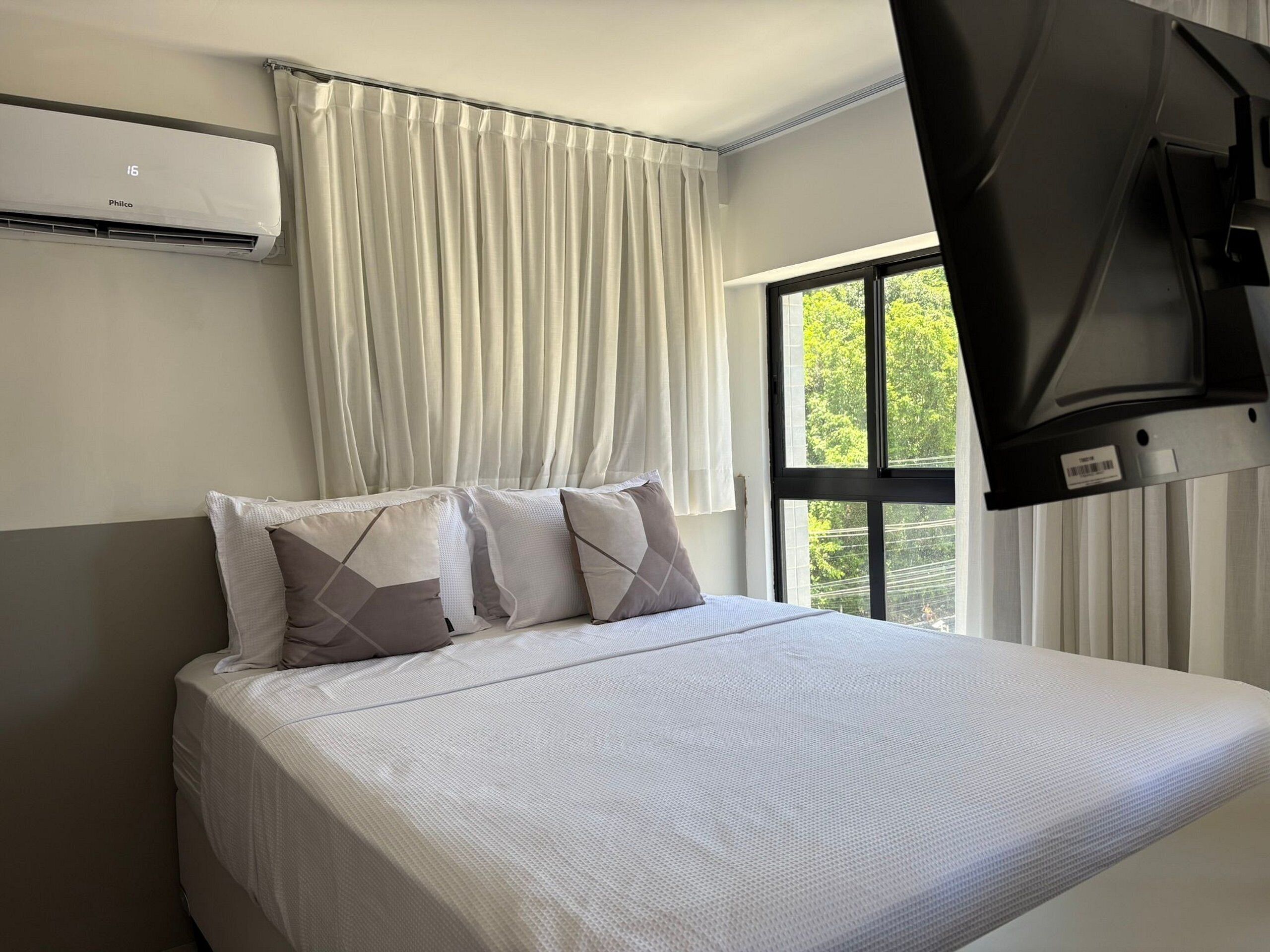 A hotel room with a bed, a TV mounted on the wall, and a window with curtains.