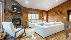 Ein gemütliches Blockhaushaus-Interieur mit Kamin aus Stein, einem Flachbildfernseher, einer Couch und Holzboden.