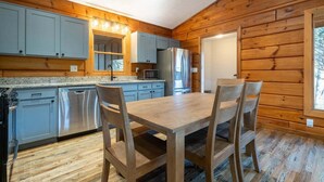 A log cabin kitchen with a wooden table and chairs, stainless steel appliances, and a window. - Cozy 3-bedroom cabin w/WiFi, Hot tub & Sauna in serene Cherry Log/ Blue Ridge (Cherry Log)