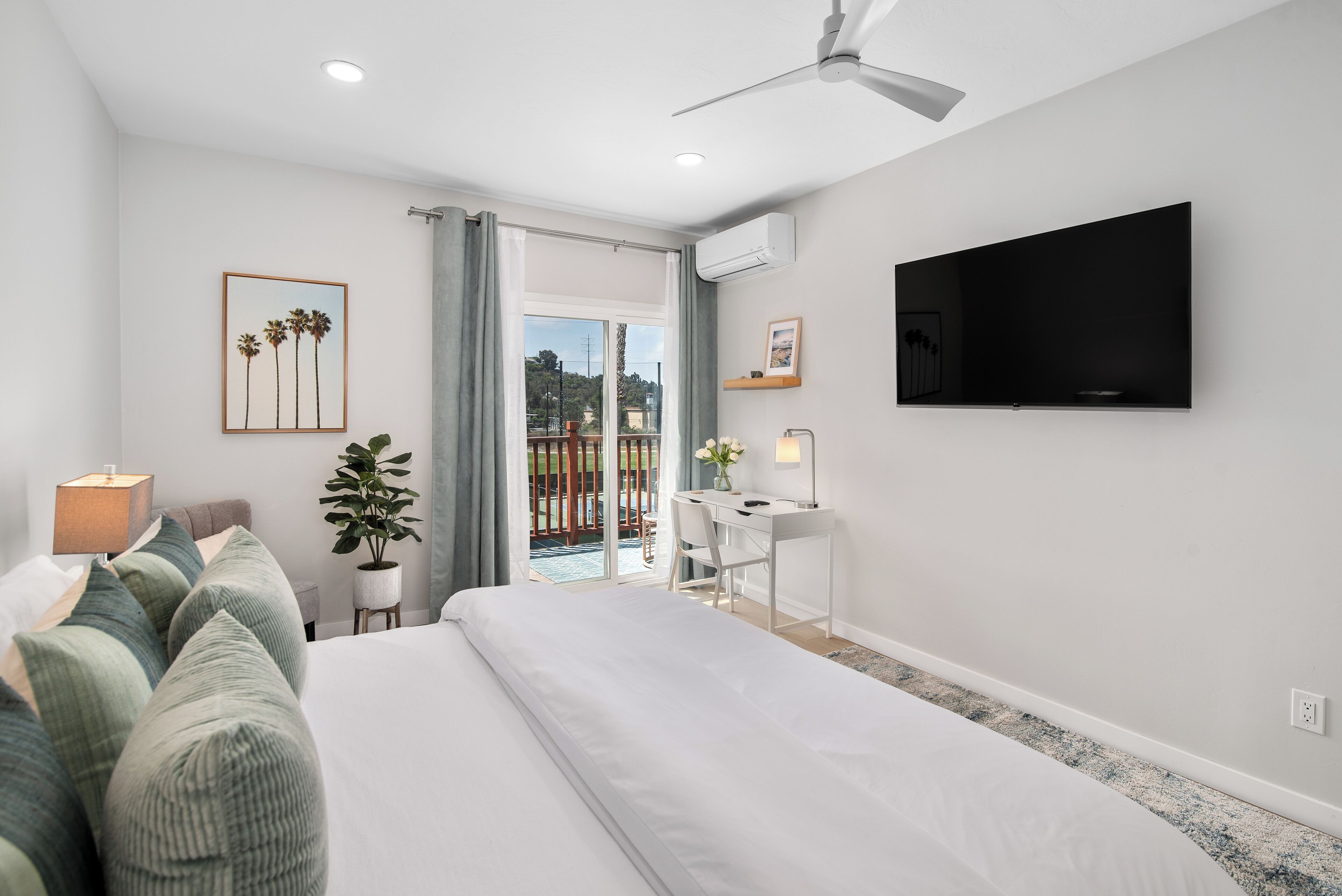 A modern hotel room with a large bed, a desk, a TV, and a balcony with a view.