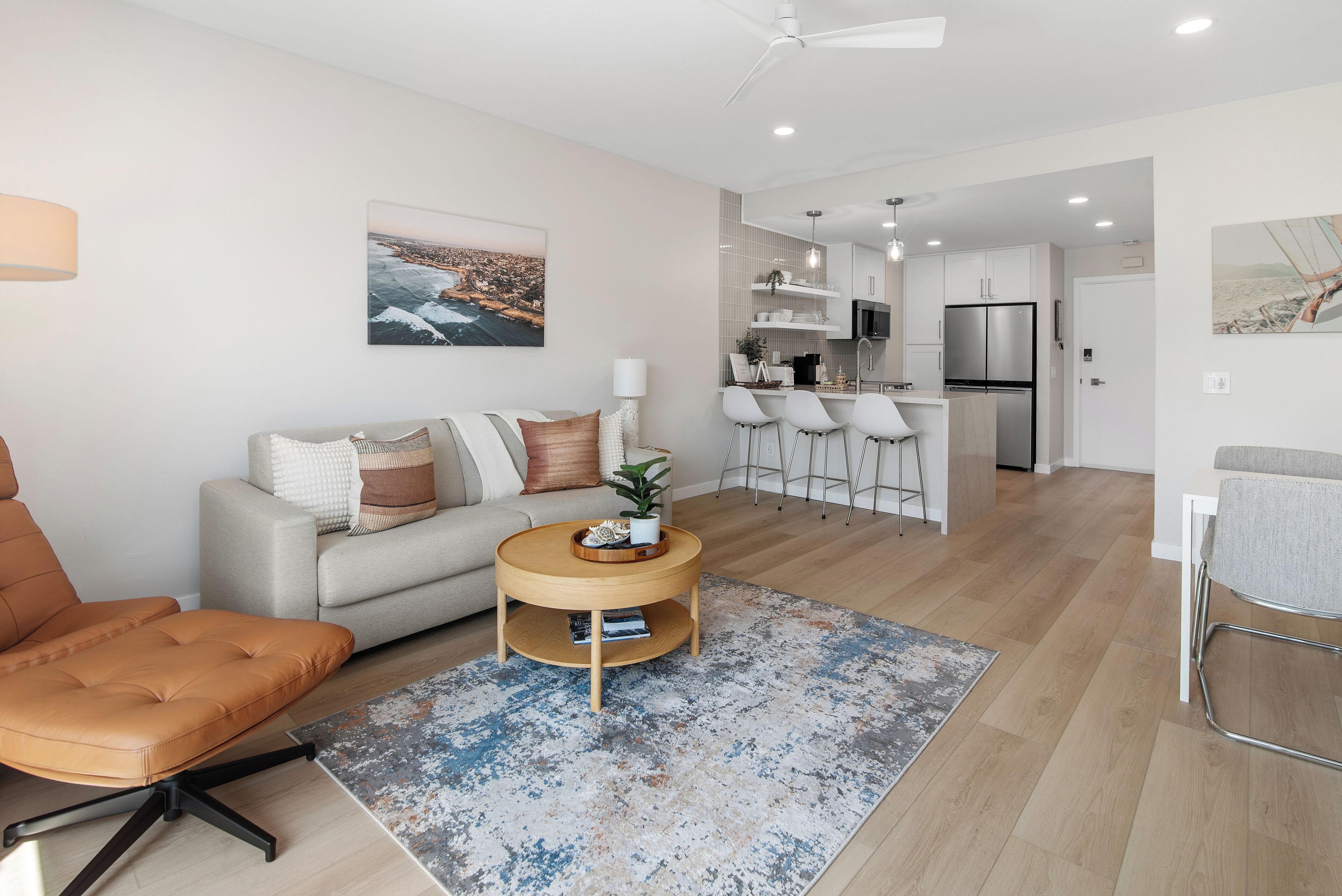 A modern living room with a sofa, armchair, coffee table, and a view of the kitchen and dining area.