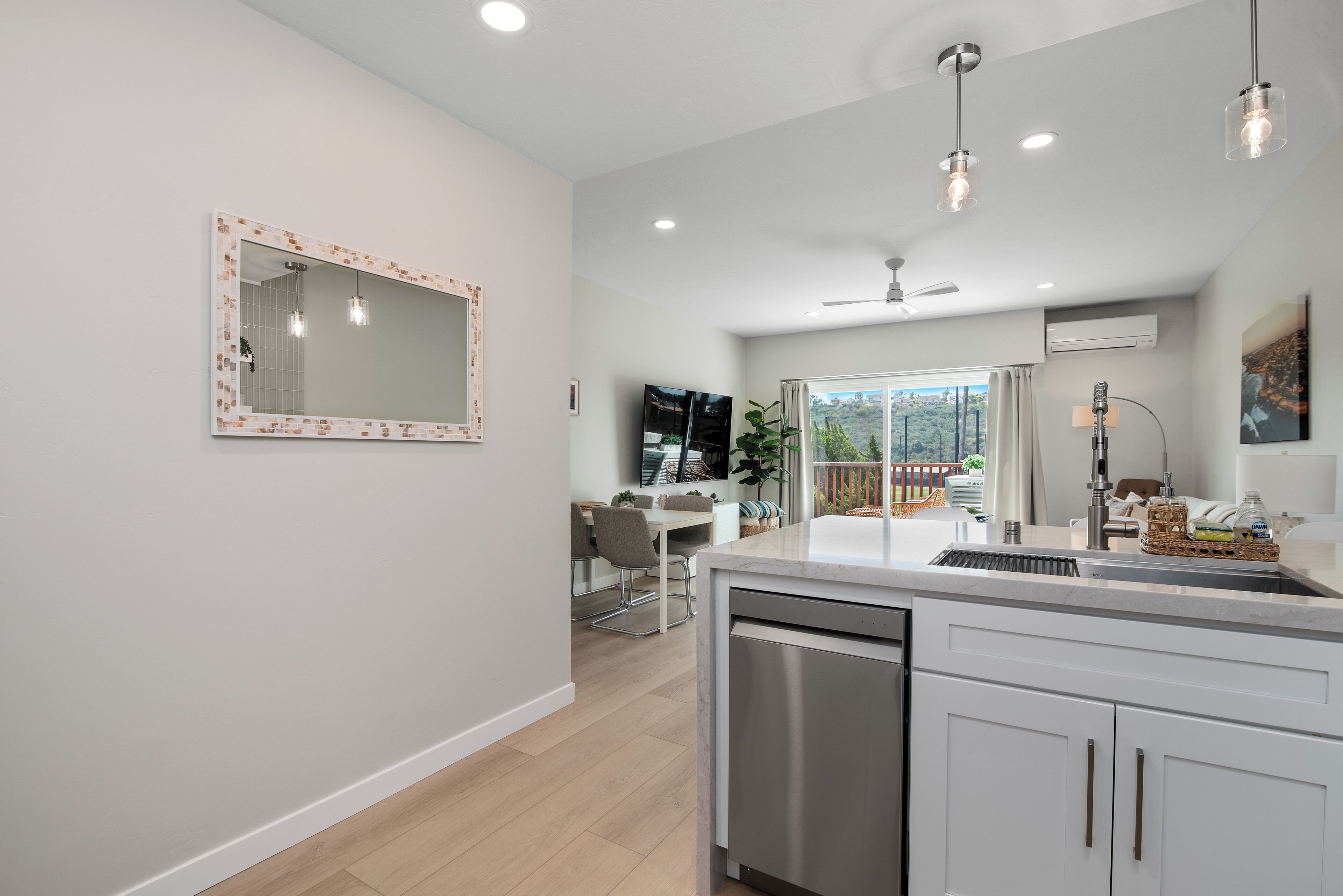 A modern kitchen with a dishwasher, a dining area with a table and chairs, and a large window offering a view of the outdoors.