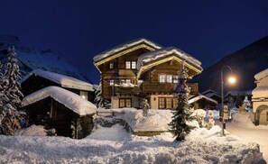 A large wooden chalet with multiple balconies, surrounded by snow-covered trees and a mountain backdrop. - Luxury Alpine Escape, Matterhorn Chalet 1012 (Valais)