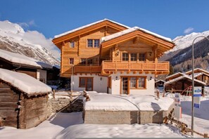 Een houten chalet met een balkon, omgeven door besneeuwde bergen.