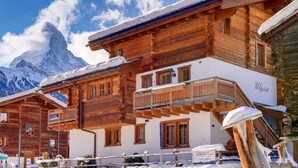 Eine Holzchalet mit Balkon, vor einer verschneiten Berglandschaft.