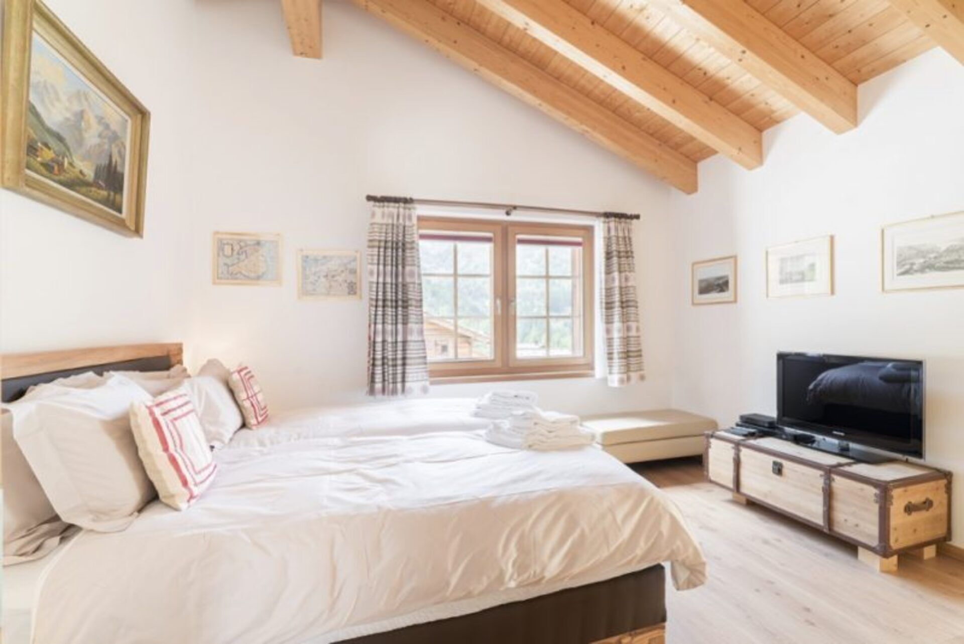 A bedroom with a bed, a TV, and a window with curtains.
