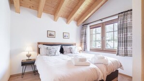 Ein Schlafzimmer mit Holzboden, einem großen Bett mit weißer Bettwäsche, zwei Nachttischen mit Lampen und einem Fenster mit Vorhängen.