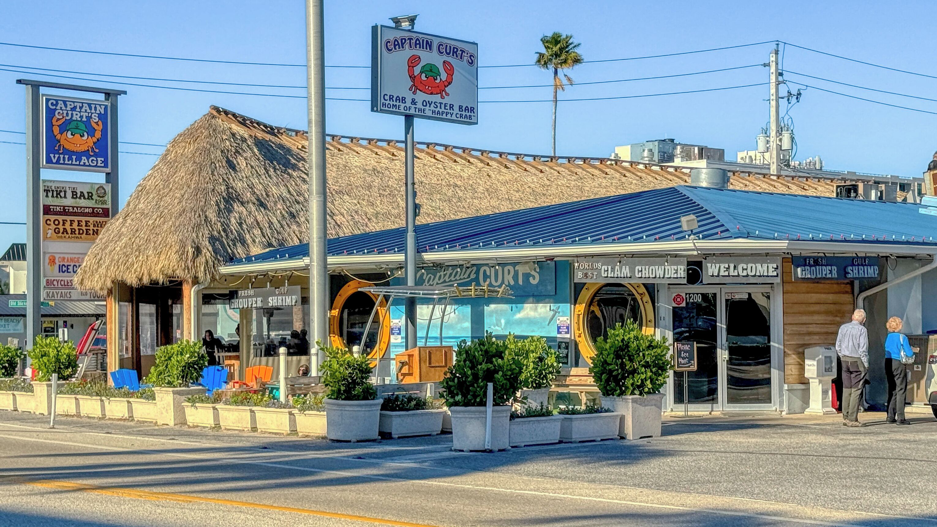 A coastal bar named Captain Curt's with a thatched roof and a sign advertising crab and oyster.
