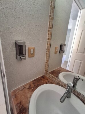 Une salle de bain avec un lavabo blanc, un miroir et un distributeur de savon fixé au mur.