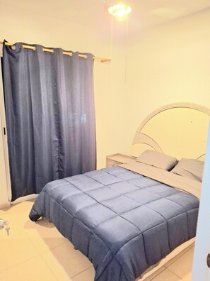 Une chambre à coucher avec un lit, une table de chevet et un rideau.