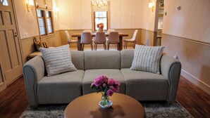 Una sala de estar con un sofá modular gris, una mesa de centro redonda de madera y un jarrón con flores rosadas.